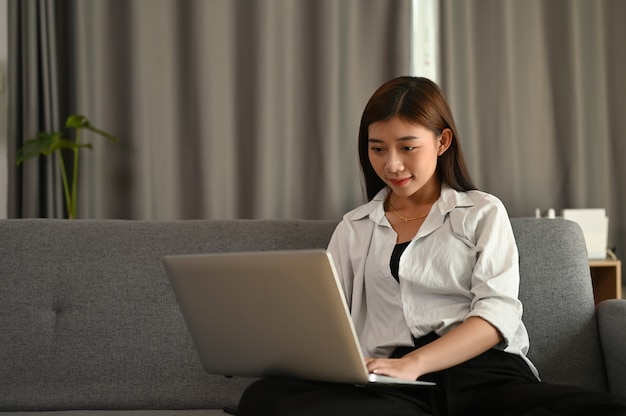 Junge asiatische Frau, die von zu Hause auf einem Laptop arbeitet