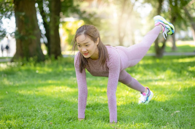 Junge asiatische Frau, die Yoga-Fitnessübungen im Naturpark macht, Übung für Gesundheit oder Aufwärmkörper, frische Luft oder Sauerstoff im grünen Baum im Park im Sonnenlicht.