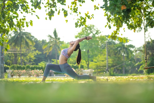 Foto junge asiatische frau, die yoga unter dem baum im park tut