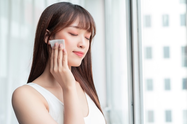 Junge asiatische Frau entfernte Make-up am Fenster