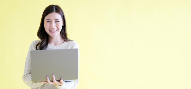 Junge asiatische Frau hält einen Laptop, lächelt und blickt in die Kamera