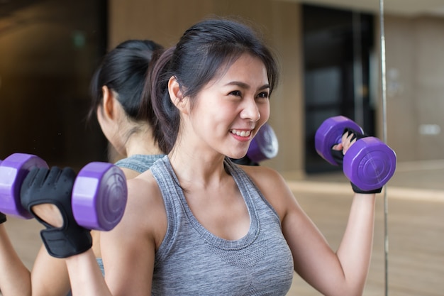 Junge asiatische Frau hält Hanteln im Fitnessstudio