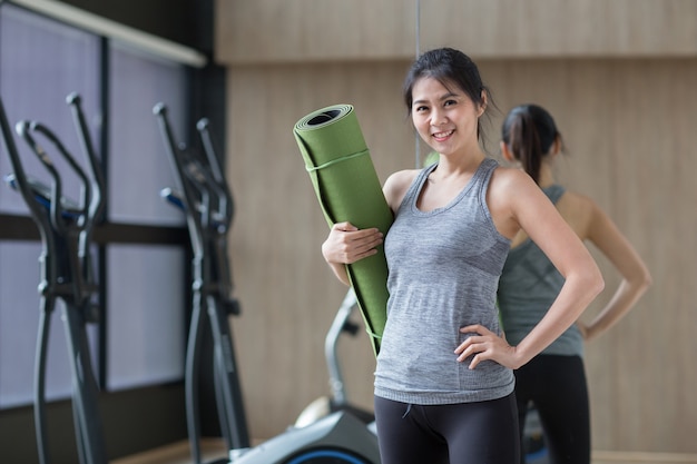 Junge asiatische Frau hält Yogamatte im Fitnessstudio