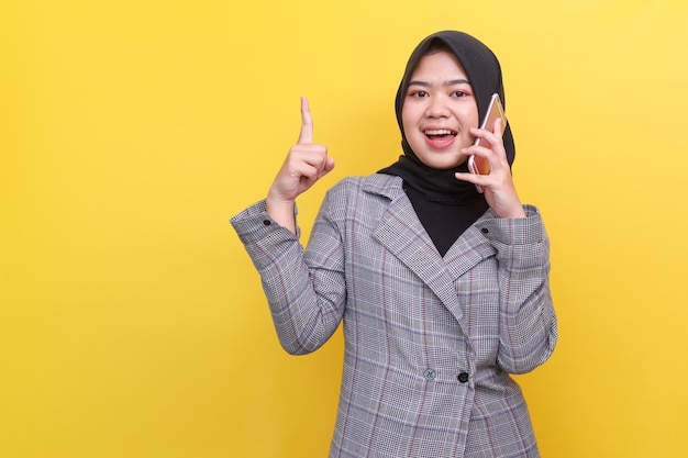 Junge asiatische Frau im Hijab, die sich unterhält, auf dem Smartphone spricht und mit dem Finger nach oben zeigt