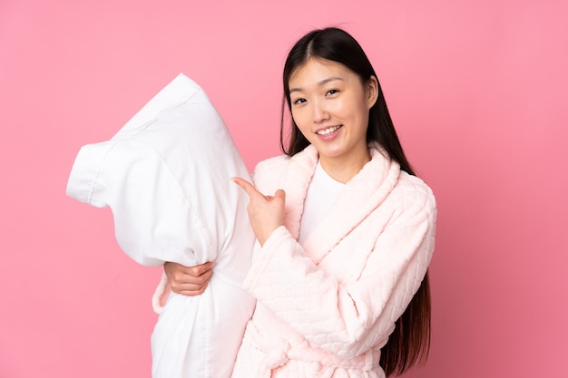 Junge asiatische Frau im Pyjama auf rosa Wand und zeigt es