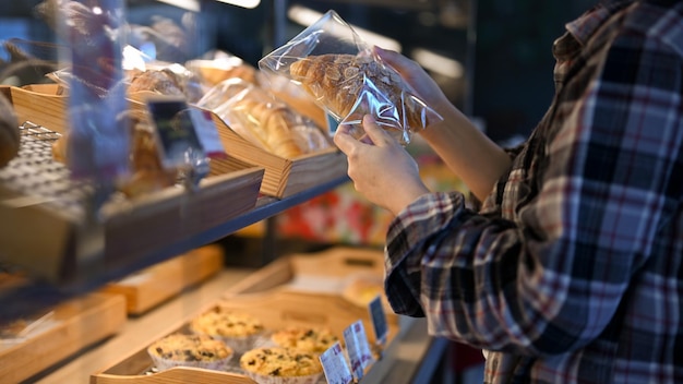 Junge asiatische Frau in der Bäckerei, die ein Croissant-Schnittbild sucht und auswählt