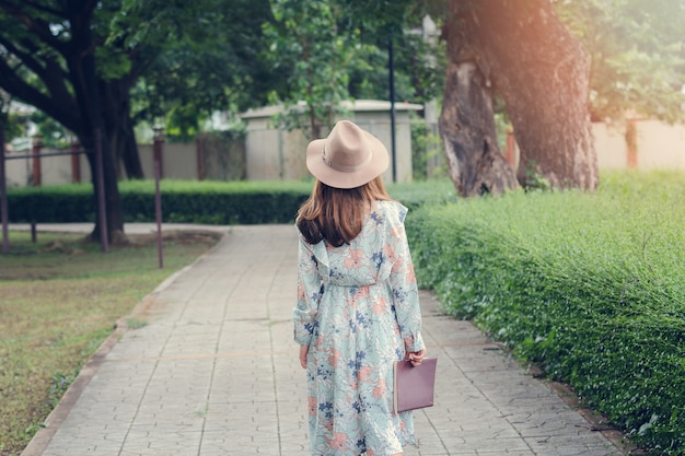 Junge asiatische Frau in der Retro- Art mit einem Buch, das in Park schlendert