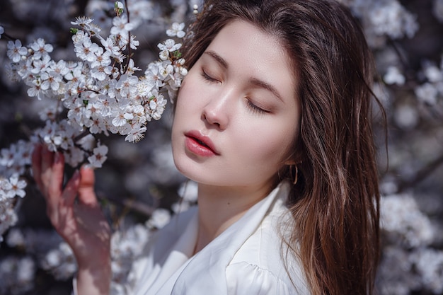 Junge asiatische Frau in einem blühenden Garten. romantisches bild einer stylischen lässigen frau, trendige seidenbluse. positive Stimmung. Cheery Blossom voller Blüte in Japan.