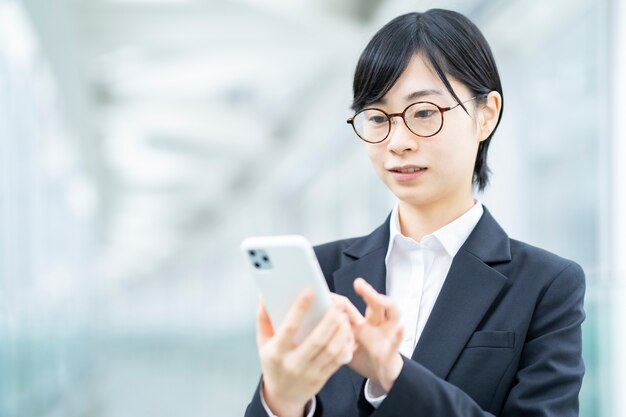 Junge asiatische Frau in einem professionellen Anzug mit Smartphone