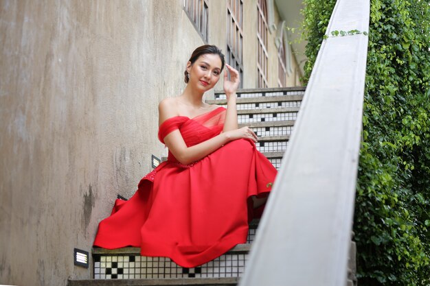 Junge asiatische Frau in einem schönen roten Kleid, das Kamera mit Lächeln betrachtet. Modemodell, Braut oder Vorhochzeitskonzept.