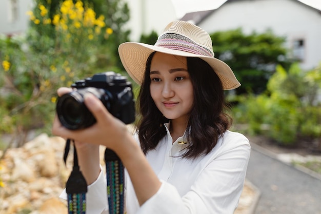 Junge asiatische Frau in weißem Hemd und Hut in einem Park lächelnd mit Kamera Hobby- oder professionelles Fotografiekonzept Frühlings- oder Sommerzeit Outdoor-Porträt