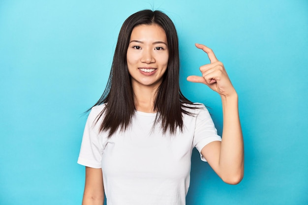 Junge asiatische Frau in weißem T-Shirt in einem Studio, die etwas Kleines mit den Zeigefingern hält