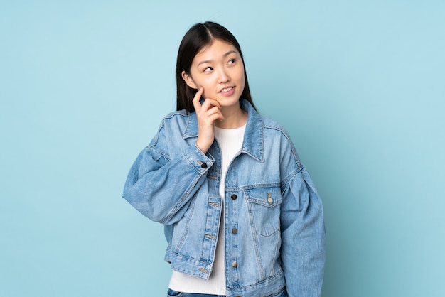 Junge asiatische Frau isoliert an der Wand, die eine Idee beim Aufschauen denkt
