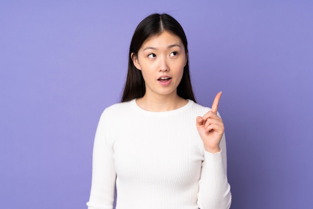 Junge asiatische Frau isoliert auf lila Raum, der eine Idee denkt, die den Finger nach oben zeigt