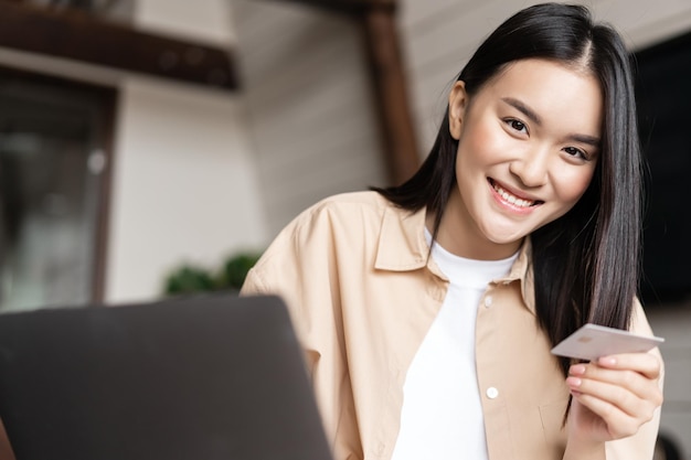 Junge asiatische Frau kauft Online-Shopping von zu Hause aus mit Laptop und Kreditkarte und lächelt...