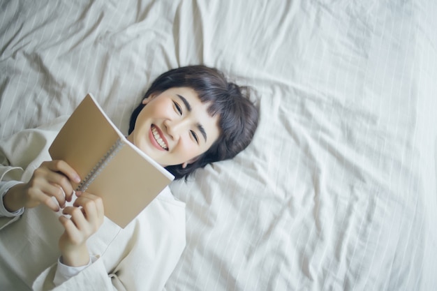 Junge asiatische Frau liest ein Buch im Schlafzimmer.