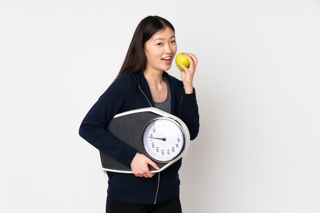 Junge asiatische Frau lokalisiert auf weißem Raum mit Waage und mit einem Apfel