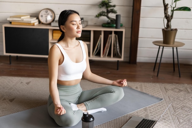 Junge asiatische Frau macht Yoga mit Laptop und hört Meditationslehrer auf Antrag oder Website...