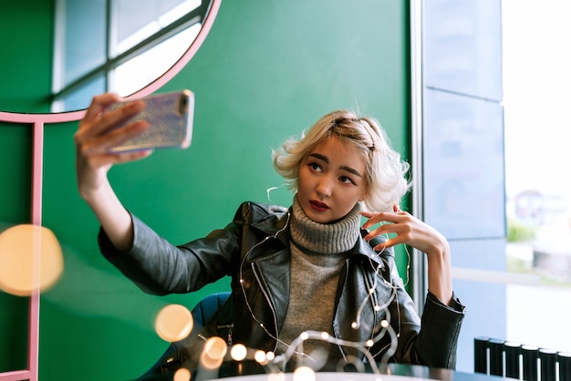 Junge asiatische Frau mit blondem Haar, das Selfie mit Lichterketten macht