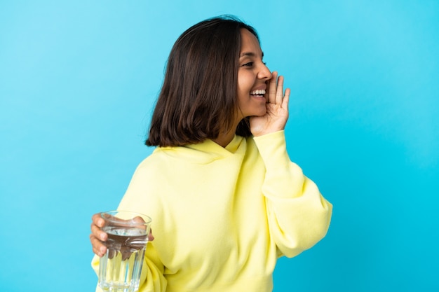 Junge asiatische Frau mit einem Glas Wasser auf blauem Schreien mit weit offenem Mund zur Seite