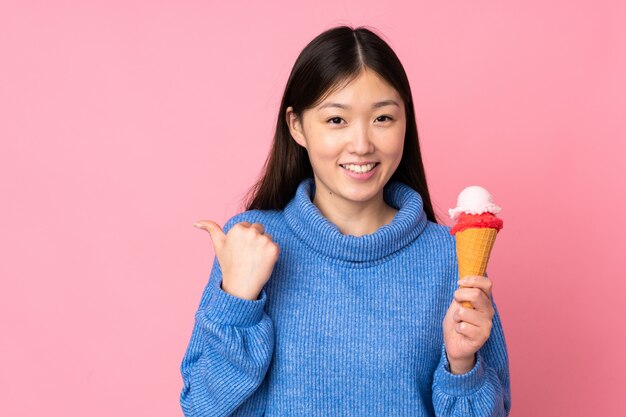 Junge asiatische Frau mit einem Kornetteis auf rosa Wand, die zur Seite zeigt