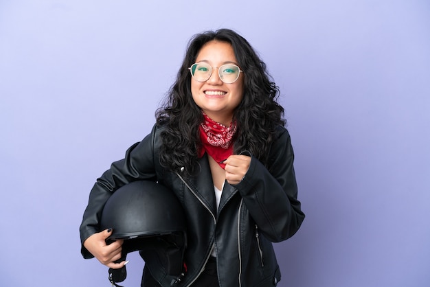 Junge asiatische Frau mit einem Motorradhelm auf violettem Hintergrund isoliert einen Sieg in Siegerposition feiernd