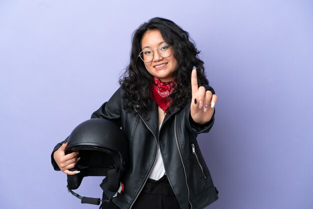 Junge asiatische Frau mit einem Motorradhelm isoliert auf lila Hintergrund, der einen Finger zeigt und hebt