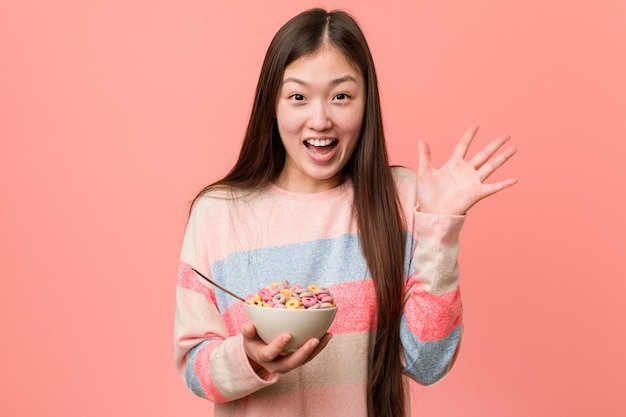 Junge asiatische Frau mit einer Müslischüssel einen Sieg oder einen Erfolg feiernd