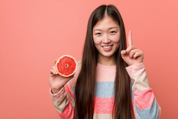 Junge asiatische Frau mit einer Pampelmuse, die Nummer Eins mit dem Finger zeigt.