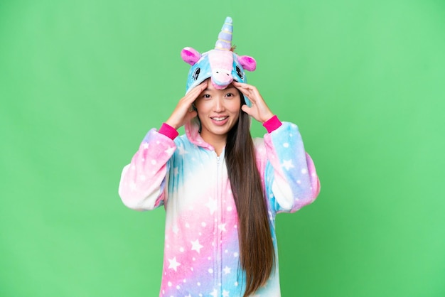 Junge asiatische Frau mit Einhorn-Pyjama vor isoliertem Chroma-Key-Hintergrund mit überraschendem Gesichtsausdruck