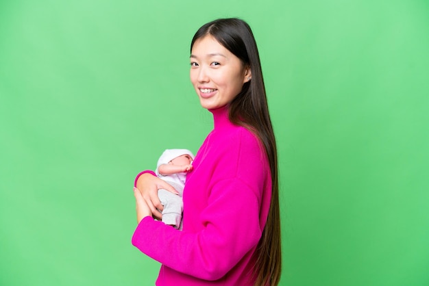 Junge asiatische Frau mit ihrem neugeborenen Baby über isoliertem Chroma-Key-Hintergrund lächelt viel