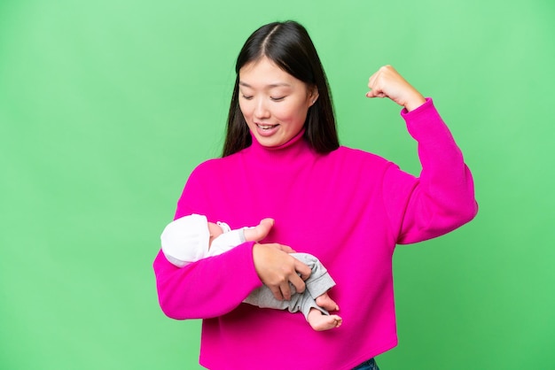 Junge asiatische Frau mit ihrem neugeborenen Baby vor isoliertem Chroma-Key-Hintergrund feiert einen Sieg