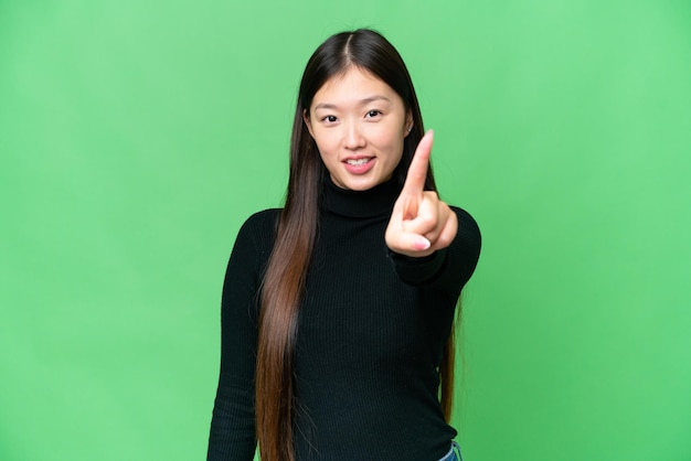 Junge asiatische Frau mit isoliertem Chroma-Key-Hintergrund zeigt und hebt einen Finger