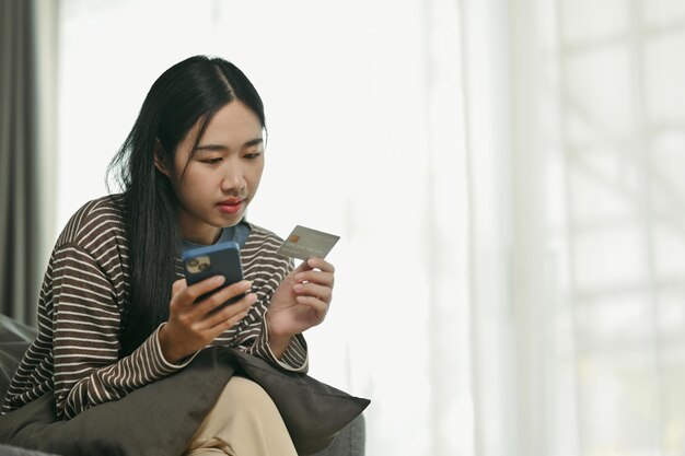 Junge asiatische Frau mit Kreditkarte und Online-Banking-Transaktion auf Mobiltelefon