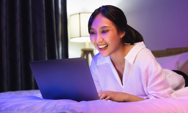 Junge asiatische Frau mit Laptop auf dem Bett im Schlafzimmer in der Hausnacht.