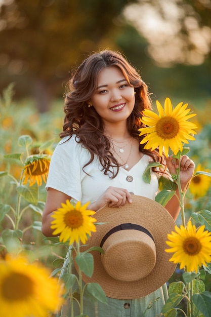 Junge asiatische Frau mit lockigem Haar in einem Feld von Sonnenblumen bei Sonnenuntergang. Porträt einer jungen schönen asiatischen Frau in der Sonne. Sommer.