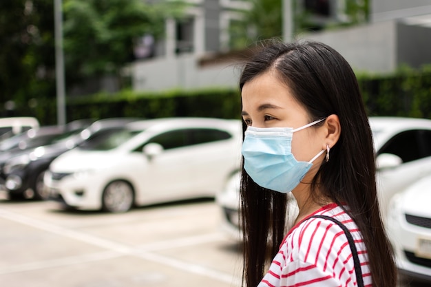 Junge asiatische Frau mit medizinischer Hygieneschutzmaske auf dem Parkplatz.