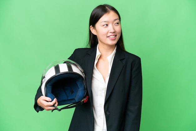 Junge asiatische Frau mit Motorradhelm vor isoliertem Chroma-Key-Hintergrund, Blickseite