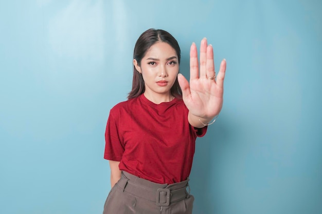 Junge asiatische Frau mit rotem T-Shirt über blauem, isoliertem Hintergrund, die mit der Handfläche ein Stoppschild macht