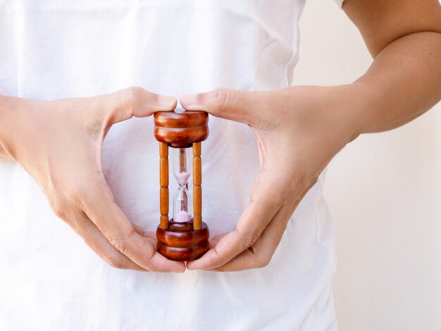 Junge asiatische Frau mit Sanduhr in der Hand am Bauch, an der Konzeptzeit von Menstruationskrämpfen und an den Magenschmerzen, am Timer im Gesundheitswesen oder am Countdown der Schwangerschaft.