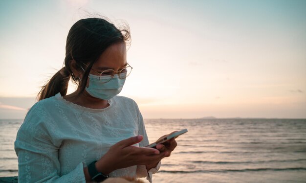 Junge asiatische Frau mit Smartphone am Strand mit Hintergrund des Bossiness-Konzepts bei Sonnenuntergang