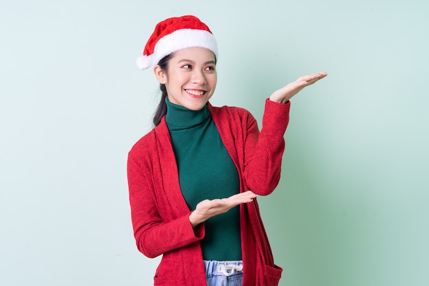 Junge asiatische Frau mit Weihnachtsmütze auf grünem Hintergrund, Weihnachtskonzept