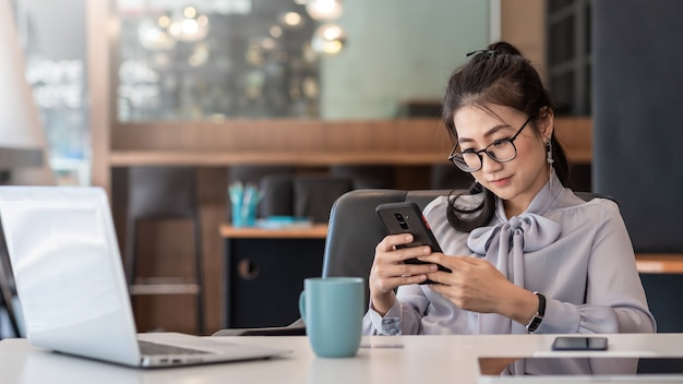 Junge asiatische Frau sind glücklich, am Telefon und am Laptop am Schreibtisch zu sitzen.