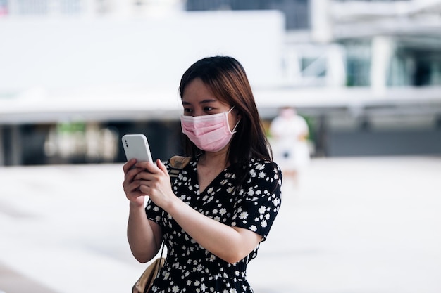 Junge asiatische Frau trägt Gesichtsmaske und benutzt Mobiltelefon in der Stadt