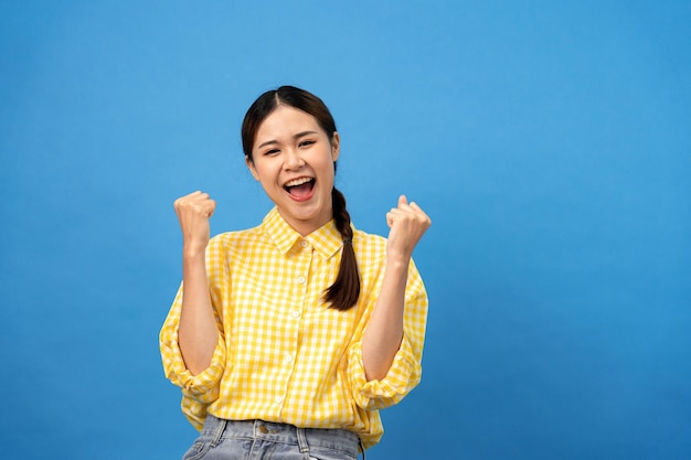Junge asiatische Frau trägt kariertes gelbes Hemd mit Zopffrisur und hebt schreiend die Arme