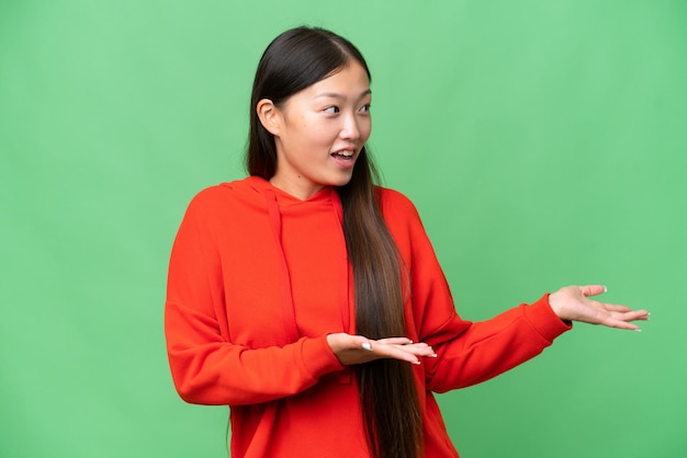 Junge asiatische Frau über lokalisiertem Hintergrund, der zurück zeigt