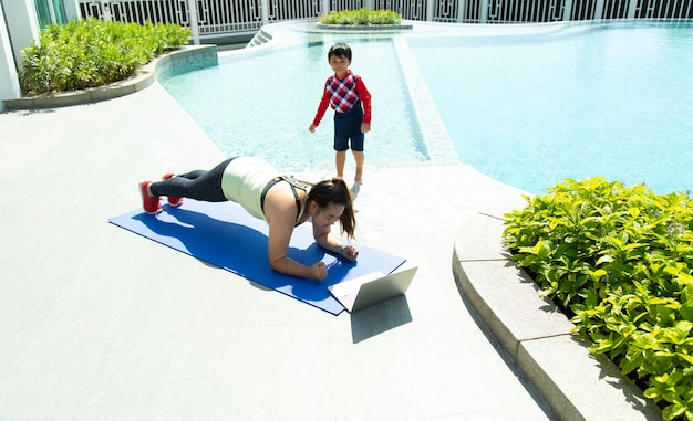 junge asiatische Frau und kleiner Junge, die lächeln, während sie auf Yogamatte Online-Training liegen. Gesunde Lebensweise und Sportkonzepte.