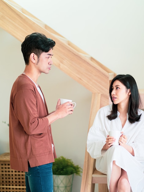 Junge asiatische Frau und Mann genießen es, Zeit zu Hause mit einer Tasse Kaffee in den Händen zu verbringen.