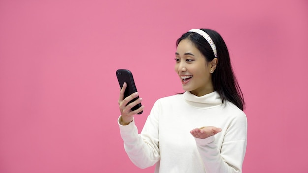 Junge asiatische frau verwendet ein intelligentes smartphone für videoanrufe auf einem rosa studiohintergrund