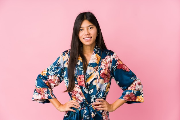 Junge asiatische Frau, welche die Pyjamas eines Kimonos überzeugt trägt, Hände auf Hüften halten.